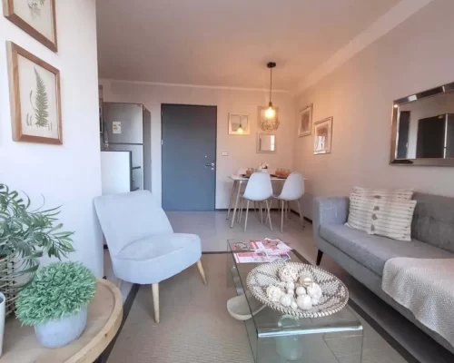 Vista del living comedor con piso de cerámica clara, paredes blancas y un ventanal que permite el ingreso de abundante luz natural.