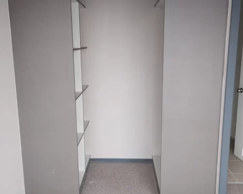 Entrada a un espacio de clóset tipo walk-in integrado en el dormitorio, con estructura lateral en melamina de color gris oscuro.