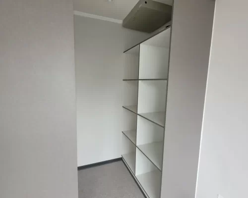 Detalle del interior de un clóset con repisas blancas organizadoras y barra metálica para colgar ropa.