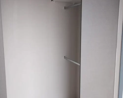 Detalle del interior de un armario con estanterías blancas y una barra metálica para colgar prendas de vestir.