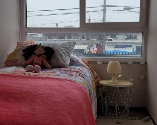 Segundo dormitorio con cama de una plaza, ropa de cama en tonos coral y ventana que permite la entrada de abundante luz natural.